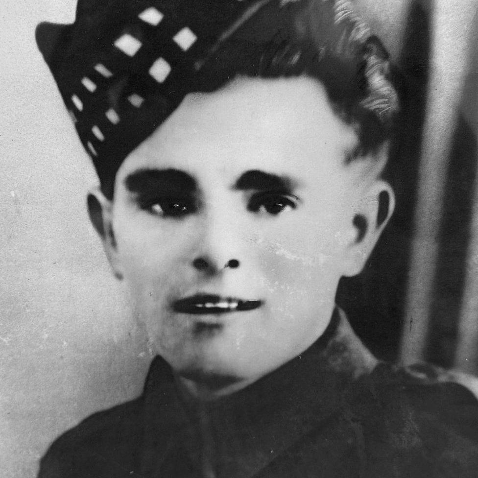 Black and white image of young man smiling at camera and wearing soldier uniform