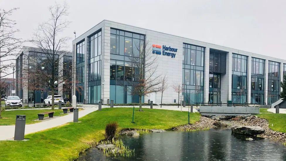 Harbour Energy building, with cars parked next to it, and a pond in the foreground.
