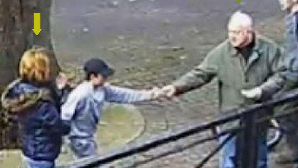 CCTV image of a boy reaching out near a duck pond take something from Sergei Skripal. Other people are walking past.