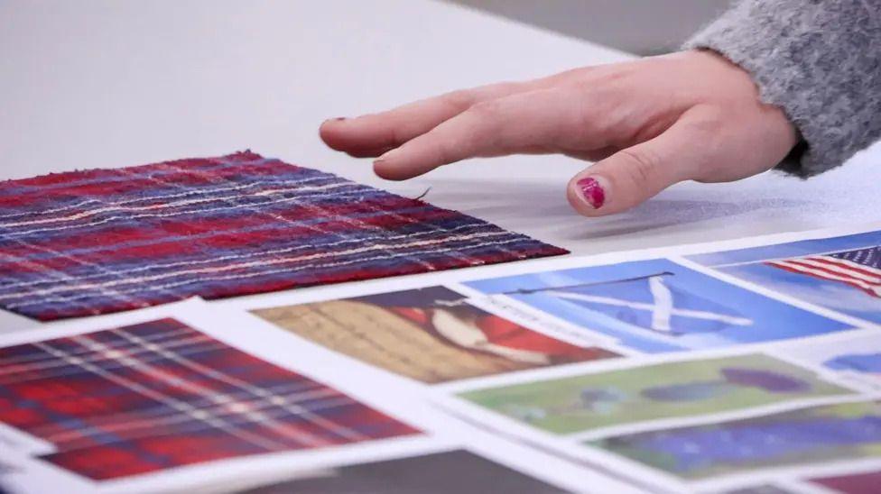 a hand hovering over different tartan patterns on a table.