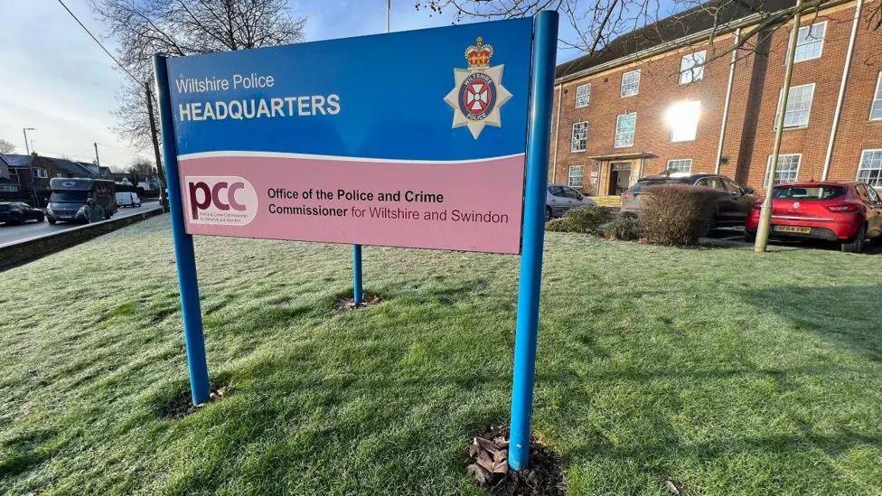 A blue sign at the Wiltshire Police Headquarters. THe building is in the background.