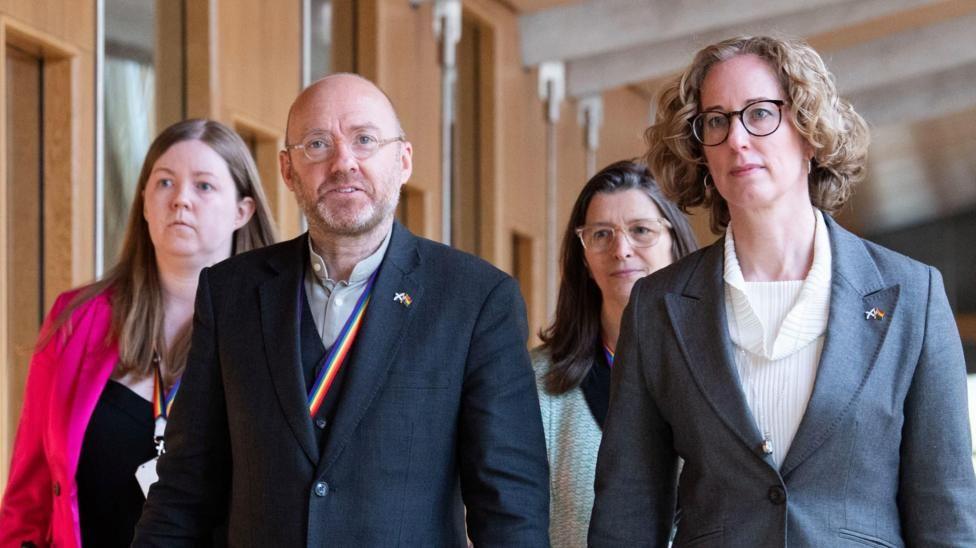 Partick Harvie and Lorna Slater walk along a corridor at holyrood with two advisors behind them