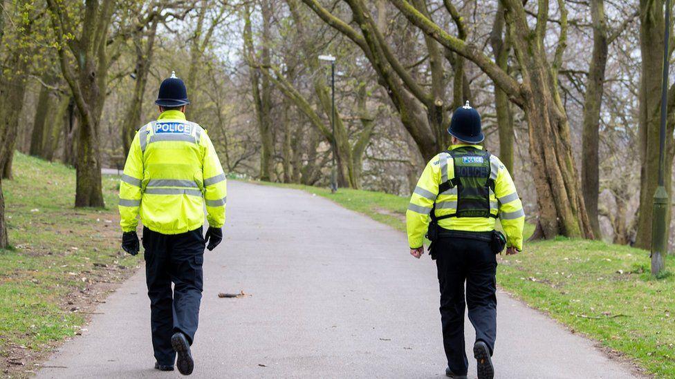 Two police officers in uniform patrol a park 