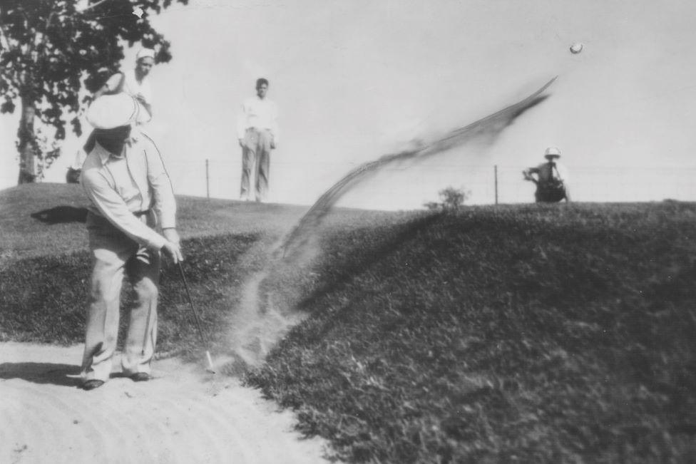 Golfer - Bobby Cruickshank - playing out of a bunker, in a black and white shot.