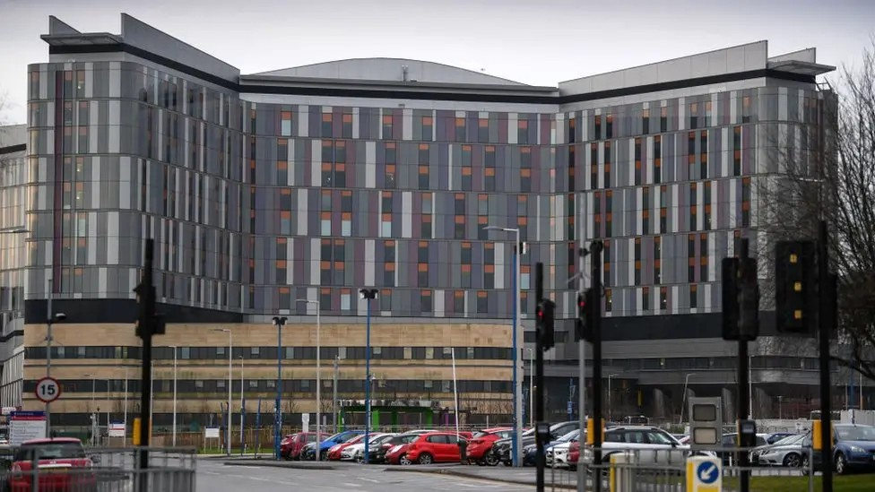 Queen Elizabeth University Hospital main building, taken from the road with traffic lights and parked cars in the foreground.