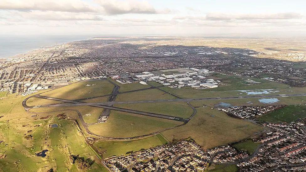 An aerial view of Blackpool Airport showing the runway, which cuts across the centre, with Blackpool and the coast in the distance