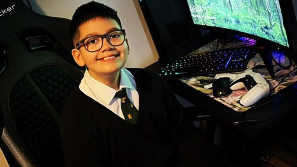 Twelve-year-old Azaan Khan in his school uniform sitting next to a computer 