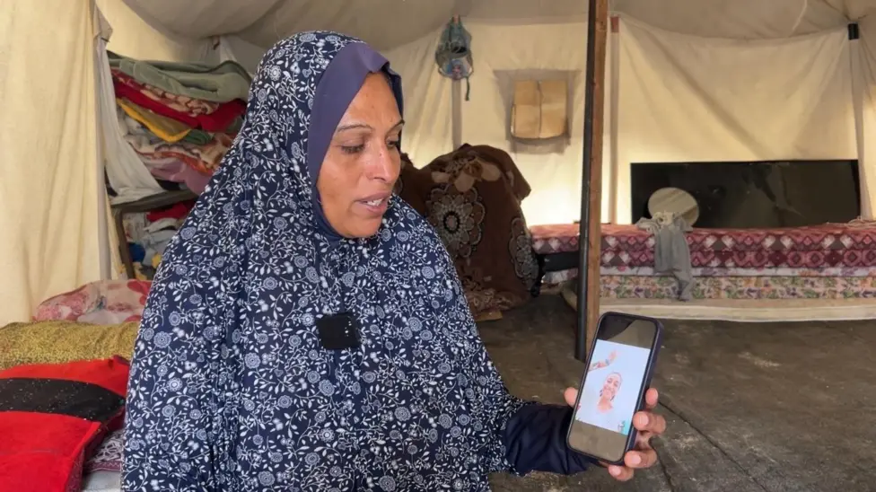 Woman in a tent holds up a photo on her mobile phone