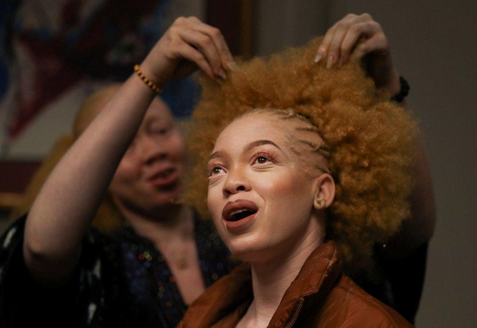 A woman smiles as she has her hair and make-up done.