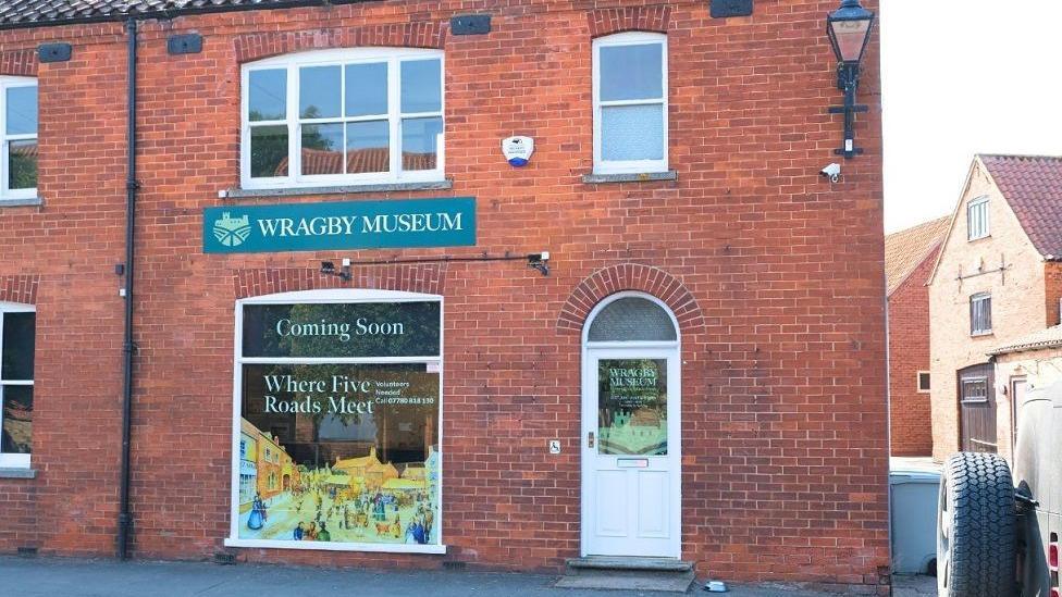 The exterior of the Wragby museum, with red bricks, a white front door and a sign saying: "Coming Soon".