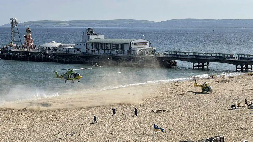 Two ambulances landing on an cleared area of Bournemouth beach with the pier in the background