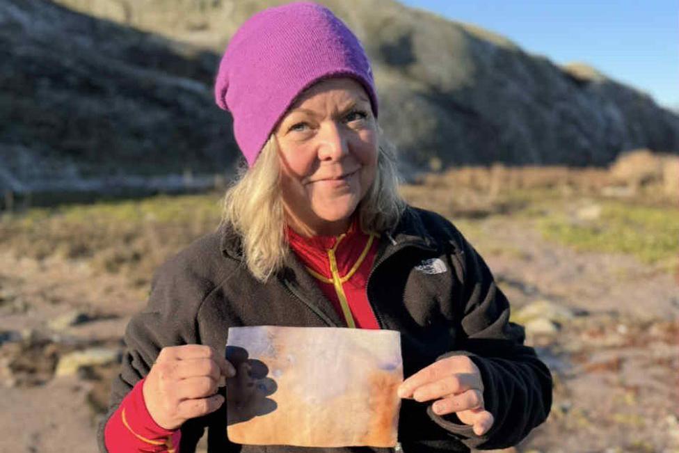 Woman - Asa Nilsson - holding an old, faded letter, she is wearing a purple hat, and a brown fleece.