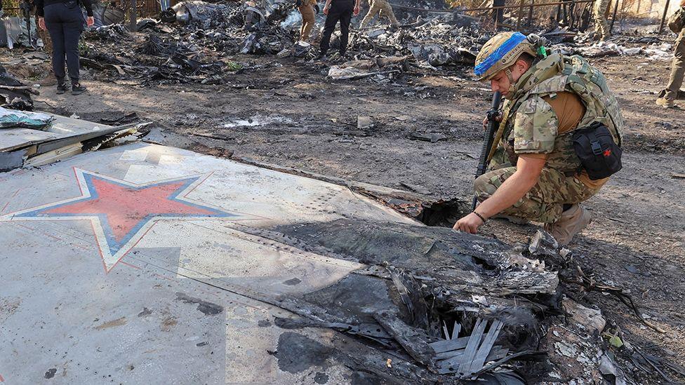 A Ukrainian service member inspects parts of a Russian aerial vehicle, which local authorities assume to be a newest heavy unmanned aerial vehicle S-70 Okhotnik (Hunter) or variation of Sukhoi fighting jet, is seen in residential area of the town of Kostintynivka