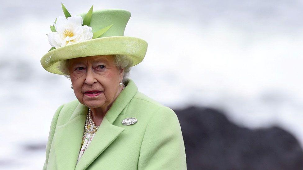 Queen Elizabeth II wears a hat adorned with a white flower and coat in pale green on a visit to Northern Ireland. 