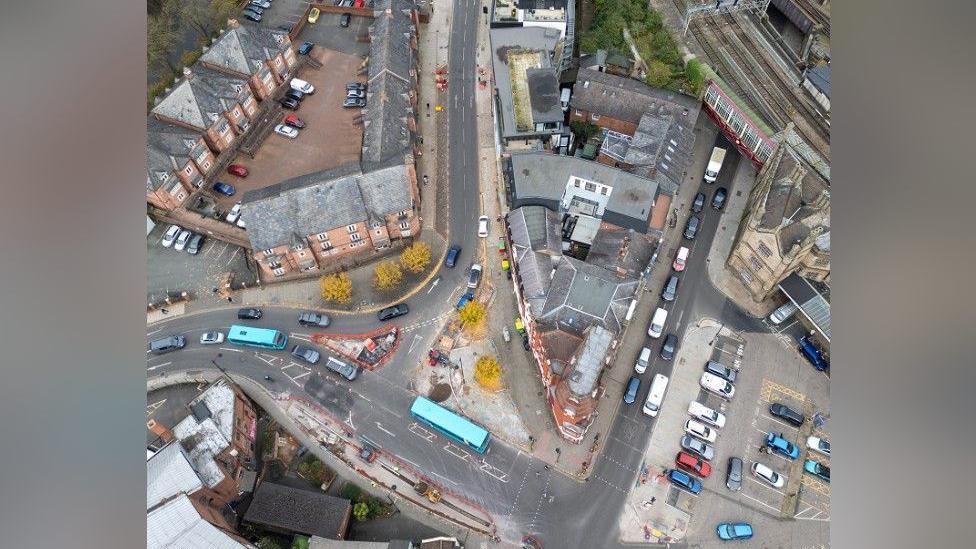 An aerial drone shot of Shrewsbury town centre. Visible is the station car park, with traffic queueing adjacent to it. There are red barriers covering an exposed area of work in a street next to it.