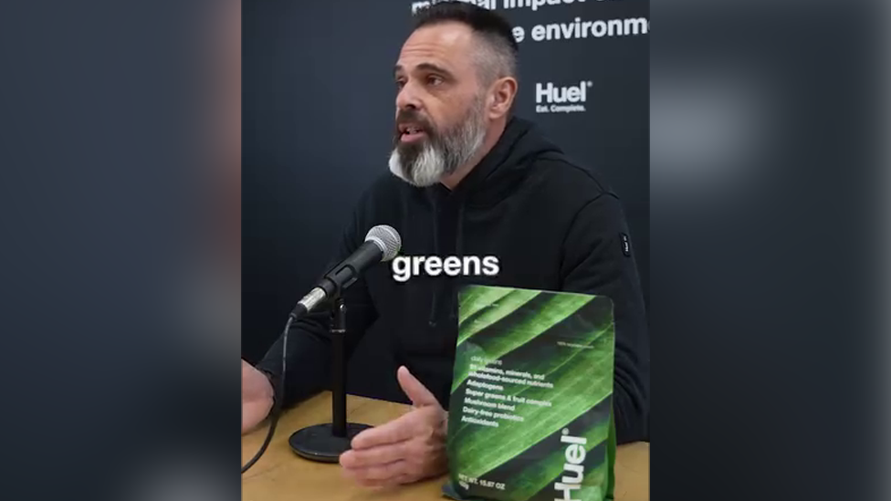 A screengrab of the banned advert on Instagram featuring a still of Julian Hearn speaking into a microphone with a bag of the product on the table next to him. Hearn has a mid-length black beard, streaked with grey and short dark hair. He has brown eyes and wears a black hoodie. 