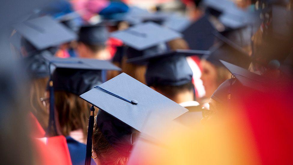 Students wearing mortarboards are gathered together at a graduation.