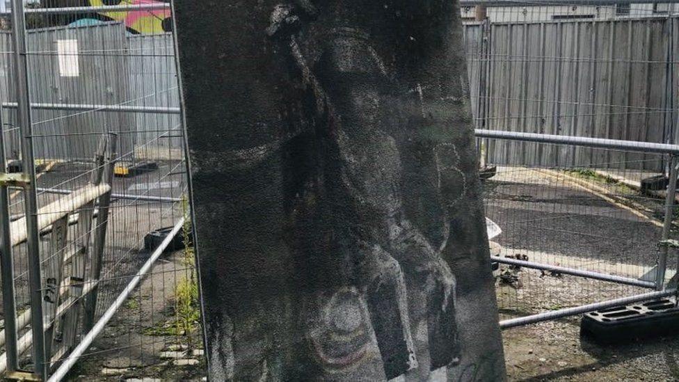 A section of the Banksy mural after it was removed from a bridge in Hull. The image has faded and is in need of repair. The section of bridge is surrounded by security fences.