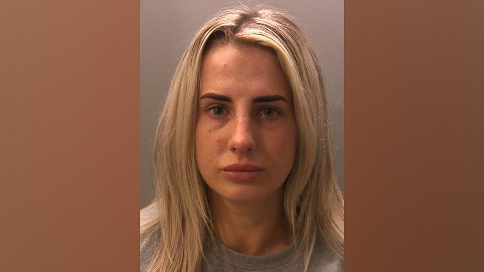 A mugshot of Jade Devine. She has blonde hair and brown eyebrows. She looks as though she has been crying.