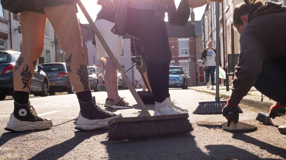 Image of residents' feet and brooms as they clean up a Middlesborough street affected by the riots in the UK