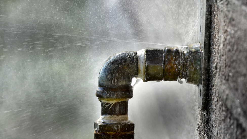 A water pipe with water leaking out of the wall