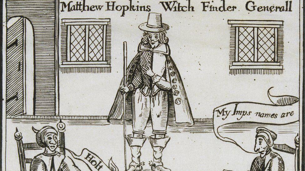 A sepia-toned 17th Century woodcut which has written at the top Matthew Hopkins Witch Finder Generall (sic). Hopkins is in the middle wearing a broad-brimmed hat, a jacket and breeches, knee-high boots and a knee-length cloak over the top. On either side of him can be seen the head and shoulders of two seated women. They are in a room with a door on the left and two windows on either side of Hopkins