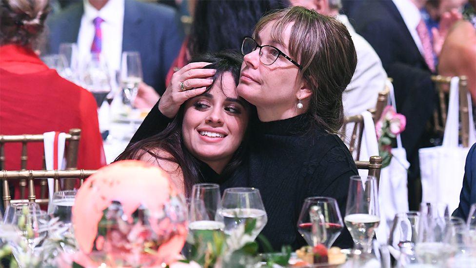 Camila Cabello and mum at a charity dinner, with Camila resting her head on her mum's shoulder, and her mum with her hand on Camila's forehead