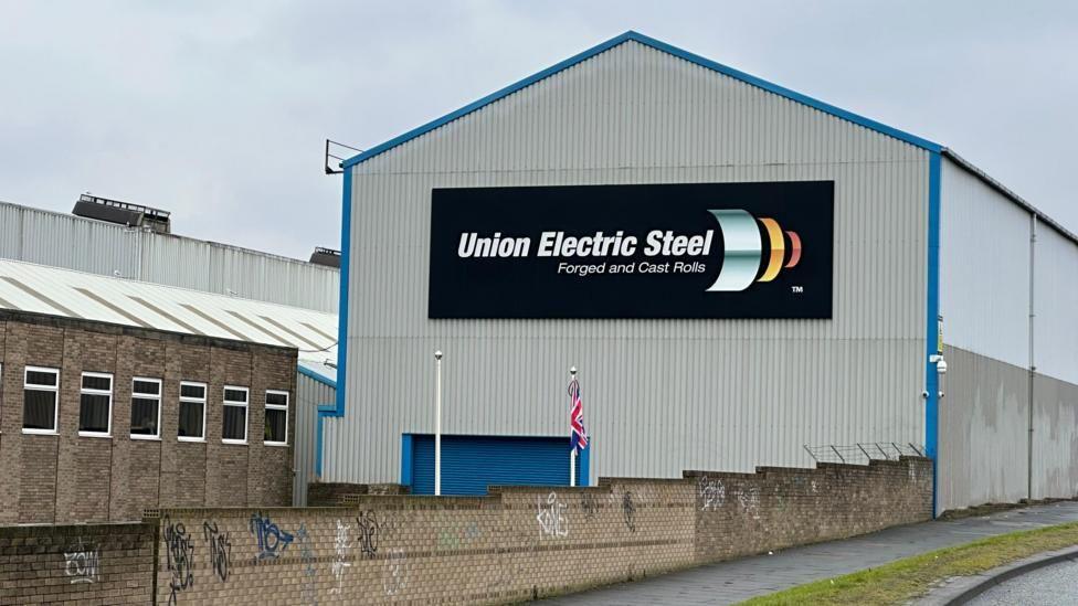The Union Electric Steel building which is a grey, corrugated building at the side of a side. It has a black sign in the centre which reads Union Electric Steel forged and cast rolls.