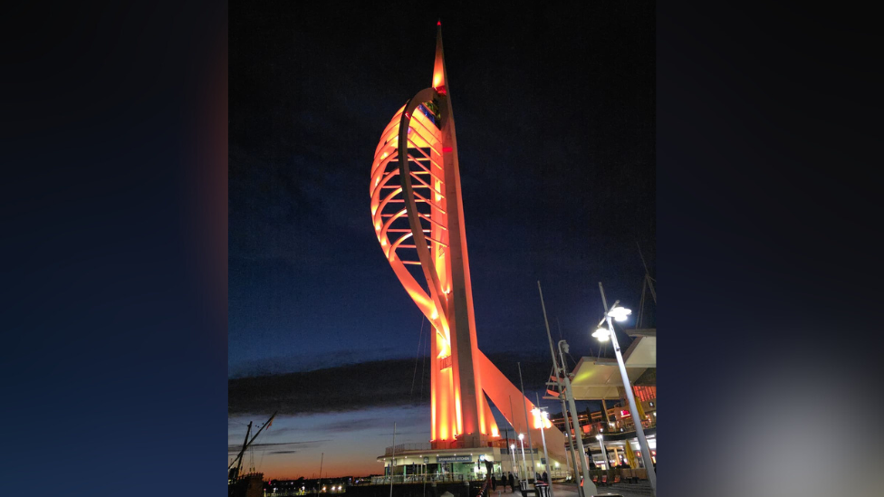 The Spinnaker Tower lit up orange as the sun sets in the distance.