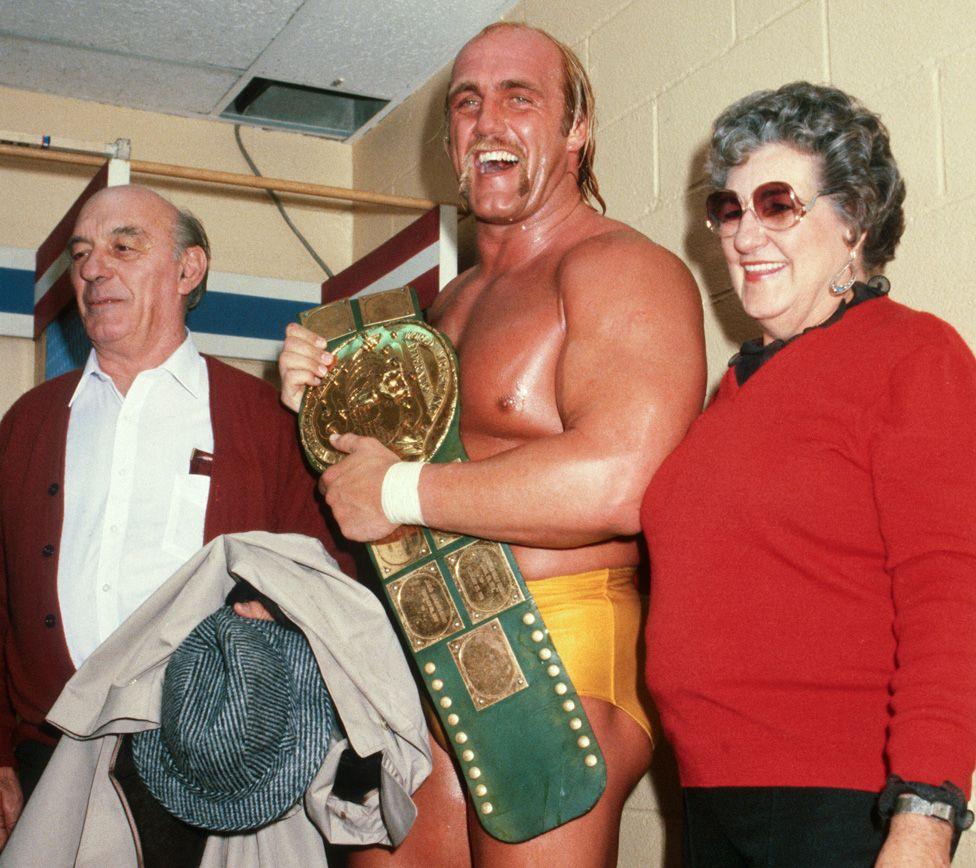 Hulk, with an open-mouthed smile, covered in sweat and holding a gold belt, standing between his parents backstage at Madison Square Garden in New York in 1984