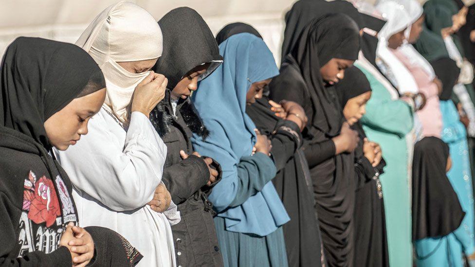 Muslim women in headscarves stand in a row with their heads bowed in prayer near Johannesburg, South Africa