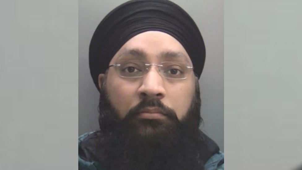 A police custody shot of a man in a turban with a beard