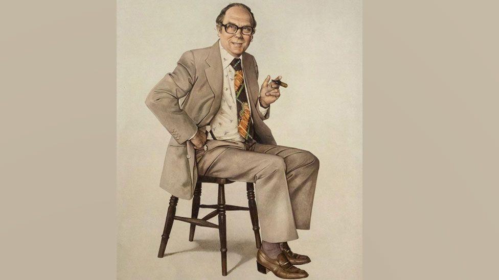 A 1978 portrait of Eric Morecambe by the artist Richard Stone. It is in sepia tones and shows the comedian sitting on a wooden chair wearing a beige suit over a white shirt with a small scattered motif and a kipper-style patterned tie. He has a cigar in his left hand and his right hand is on his hip and he is looking alert and is slightly smiling