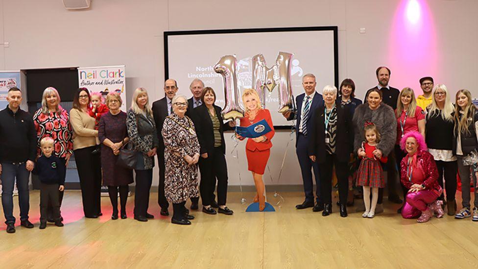 Children and adults pose with a cardboard cutout of Dolly Parton with silver balloons saying 1M at the event in Epworth