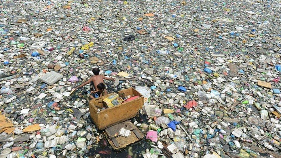 A father and son on a makeshift boat paddle through a garbage-filled river in Manila in 2015