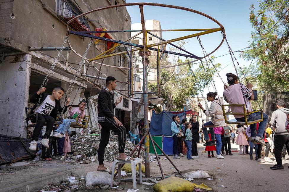 Children sit in a swing as they celebrate on the first day of the Muslim holiday of Eid al-Fitr, after the end of the holy month of Ramadan, in Deir el-Balah in the central Gaza Strip on 10 April 2024