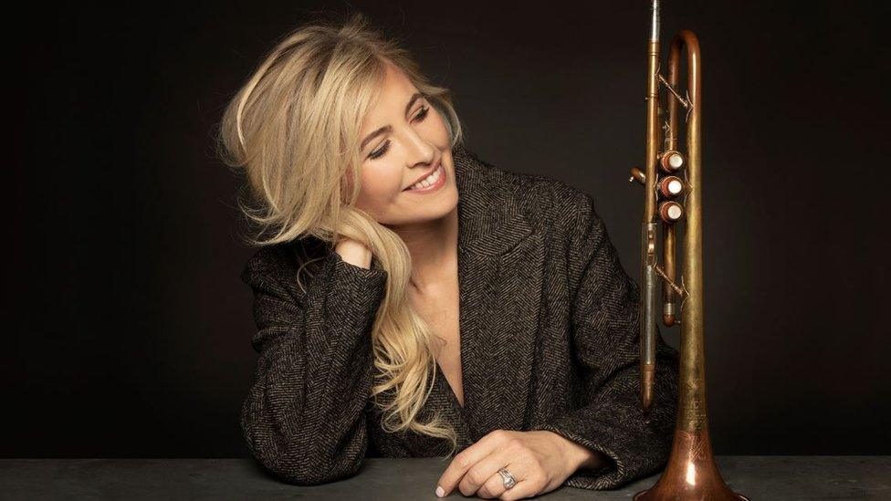 Alison Balsom sitting at a desk next to a trumpet as she looks at it.