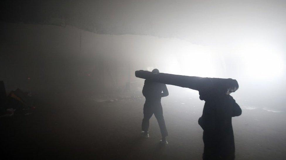 Two migrants carry a wooden railway sleeper to use as firewood inside a crumbling warehouse that has served as a make-shift shelter for hundreds of men trying to reach Western Europe in Belgrade, Serbia (12 January 2017)