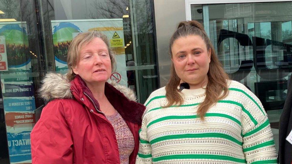 Two women, one in a red anorak and other in a green and white top, stand outside council offices