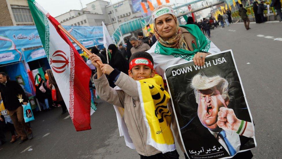 An Iranian woman holds a placard showing a caricature of US President Donald Trump being punched by a hand wearing a bracelet of the Iranian flag