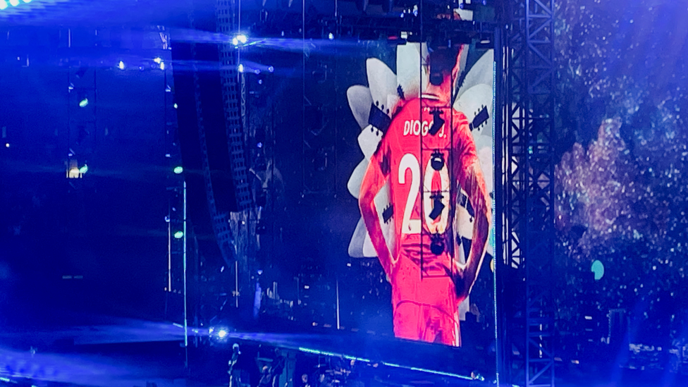 An image of the back of Diogo Jota on the big screen at the Oasis concert, wearing the number 20 on a read Liverpool shirt with Diogo J. on the back