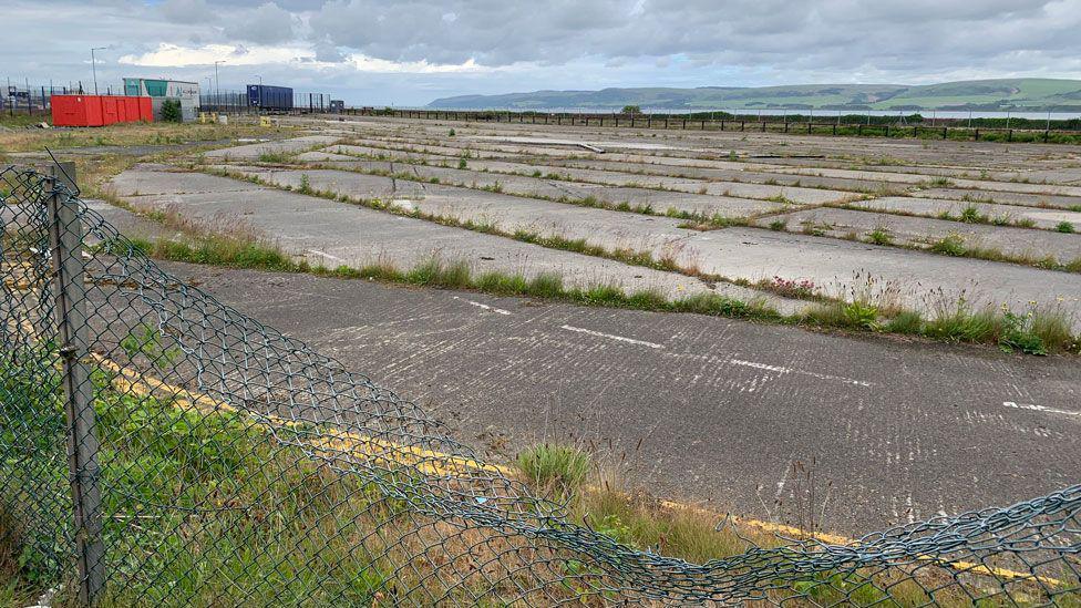 A run down piece of industrial land with tarmac and concrete and grass growing up between the cracks