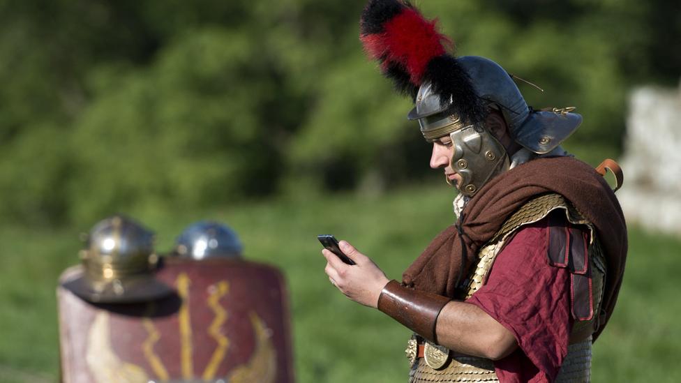 Man dressed as Roman soldier looks at mobile phone