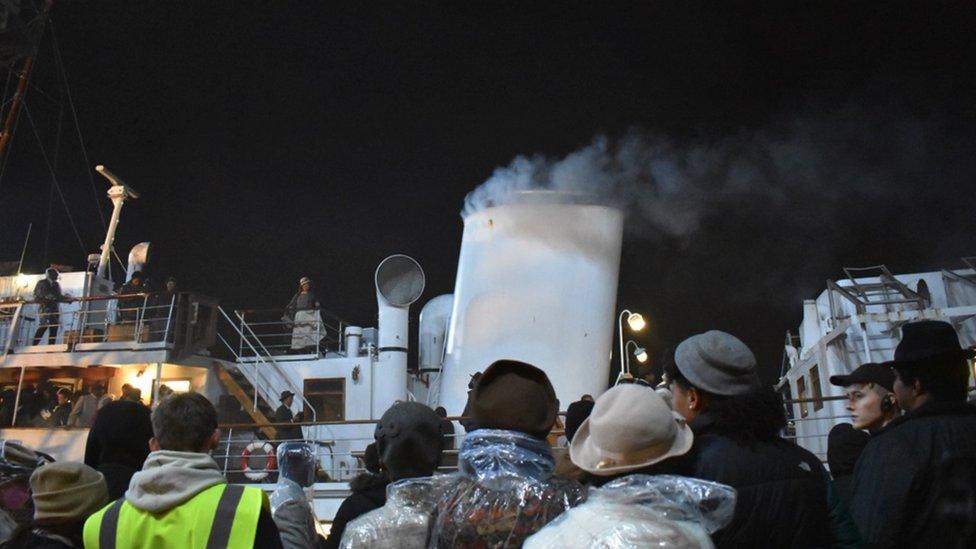 Image of the crew filming at night at Princes Wharf. Lots of people can be seen looking towards a boat.