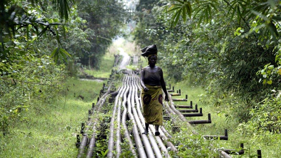 A woman walks along an oil pipeline near Shell's Utorogu flow station in Warri, Nigeria, Sunday, Jan. 15, 2006.