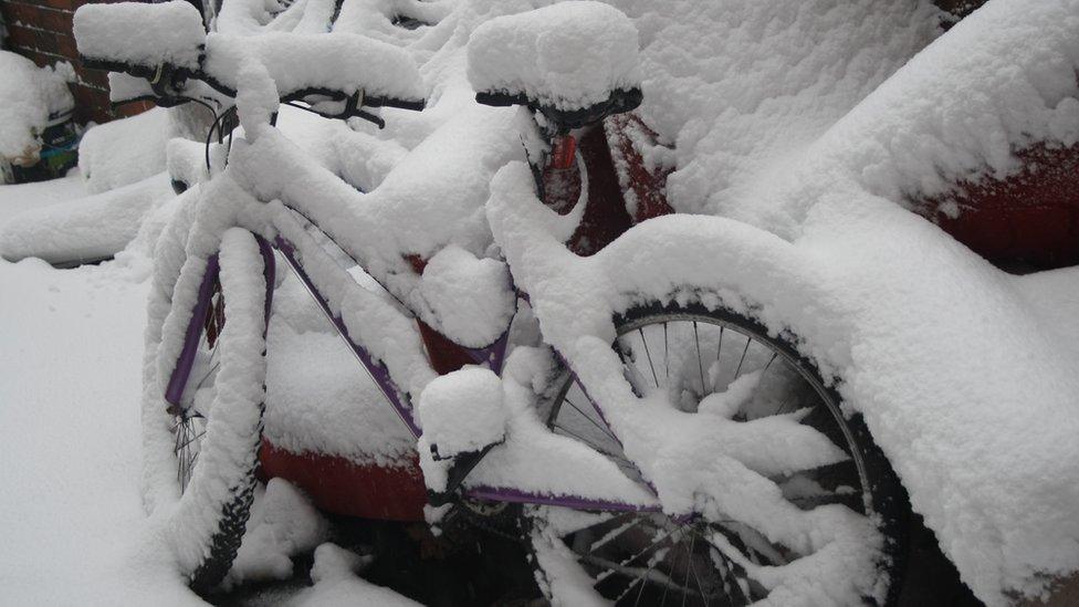 A bike covered in show leaning against a car