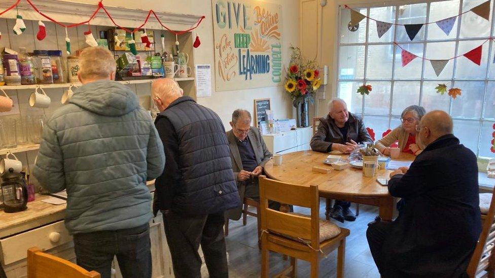 Six people sitting or standing around a table at a cafe