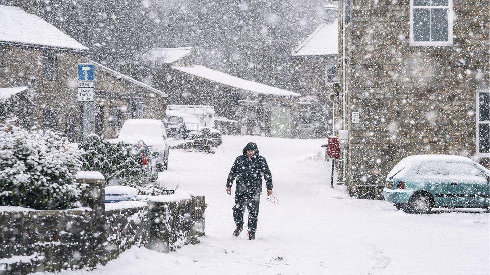 Person walks through heavy snowfall in a village