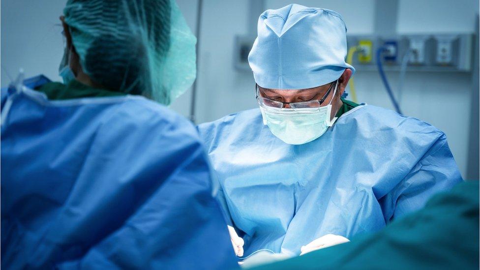 Two people in blue scrubs wearing masks in a surgery