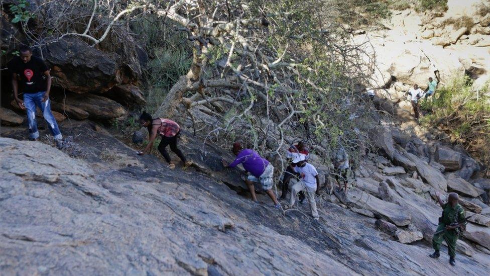 A wildlife ranger (bottom R), stands guard as local tourists (L), climb one of the cliffs that form the banks of Ewaso Nyiro river, during their visit to see the river as part of an early morning game drive through the Shaba National Reserve which is a protected area, in Isiolo, northern part of Kenya, 10 April 2016